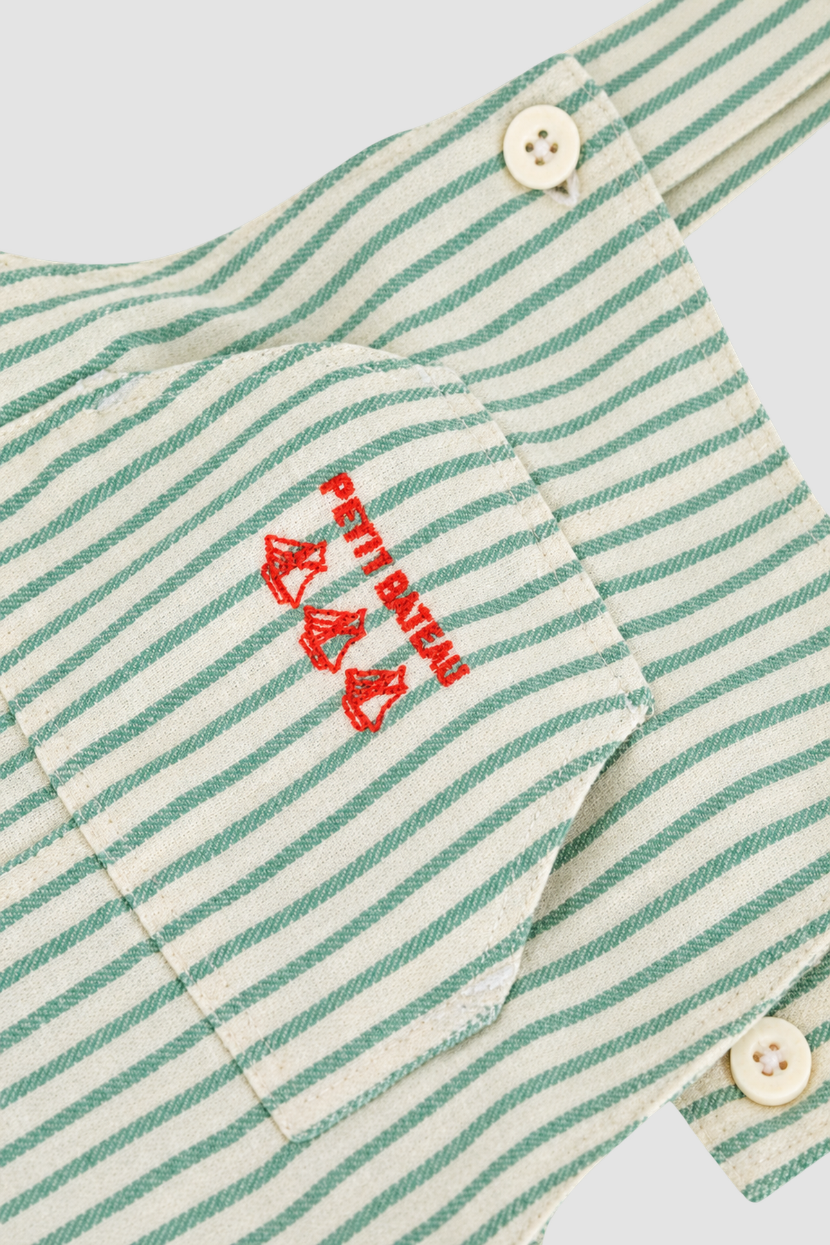 gros plan du logo brodé rouge Petit Bateau sur salopette rayée